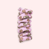 Close-up of purple spiral cat toy that has a pattern of Pusheen the Cat blushing while wearing whipped cream on her head with a tiered strawberry cake slice.