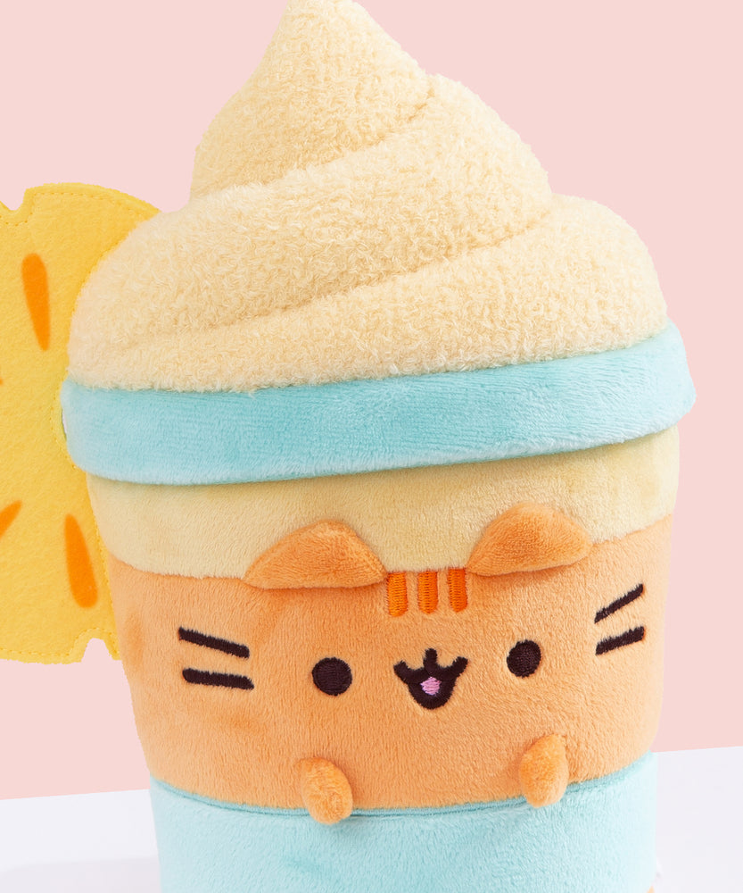 Close-up of Pineapple Float Pusheen. The medium-orange body is accompanied by blue horizontal lines to imitate a classic drink container. Pusheen's head stripes, eyes, smiling, mouth and whiskers are embroidered on the front of the plush while her orange ears and paws extend off the plush body.