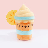 Front view of the Pusheen Fruits Pineapple Float Plush. Pusheen the Cat takes the form a delicious tropical drink served with whipped topping and a pineapple slice. The whipped topping is light orange and has a textured swirl extending off the cylinder-shaped body.