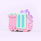 Back and side view of the Pusheen toy. The pink fuzzy dumpster sits on four legs, has side handles, and mint green top lids. On the back of the toy is Pusheen’s striped tail in alternating pink colors. Coming out of the top of the toy figure is pastel purple flames. 