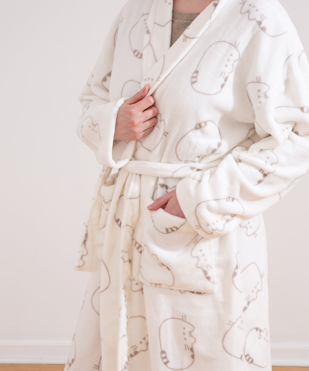 Model wearing a cream-colored Pusheen Plush robe with large all over pattern of a lying down cat. Pusheen's classic striped tail, back stripes, and facial features can be seen in full detail. 