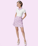 Model stands in Pusheen Purple Polka Dot Dress. The Pusheen pattern on the skirt of the dress has white polka dots and grey, laying Pusheen the Cats.  
