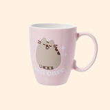 Back view of Pusheen tea mug. The light pink cup features a grey and brown graphic of Pusheen licking her paw. Around Pusheen are white sparkles and underneath the cat is the phrase “self care” in white print.