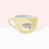 Back view of Pusheen latte mug. The light-yellow cup features a grey and brown graphic of Pusheen sleeping on a white, puffy cloud. Around Pusheen are white sparkles and above the cat is the phrase “sleepy” in white print. 