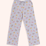 The Snack Time Pajama Pants are laid out to show the full length of the pants. The pants are covered in a pattern of Pusheen, hamburgers, French Fries, and the phrase “YUM” in pink and yellow print. 
