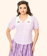 Model wears Pusheen Springtime Blouse untucked. The button closure runs down the mid front of the blouse with purple buttons that match the color of the blouse.