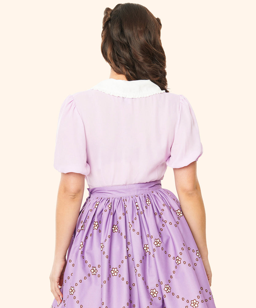 Back view of the purple blouse. The oversized white collar extends to the back of the blouse. The blouse has oversized tulip-like sleeves that end at the wearer's elbows.