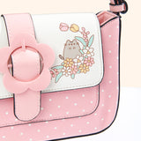 Close-up view of the Pusheen with flowers graphic on the closure flap of the Pusheen Springtime Purse. Pusheen stands in a flower bed with tulips, daisies, and green leaves.