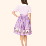 Model posed to show off the back of the Springtime Pusheen Skirt. The purple skirt falls below the model's knees and is the same length at the hem all the way around the skirt.