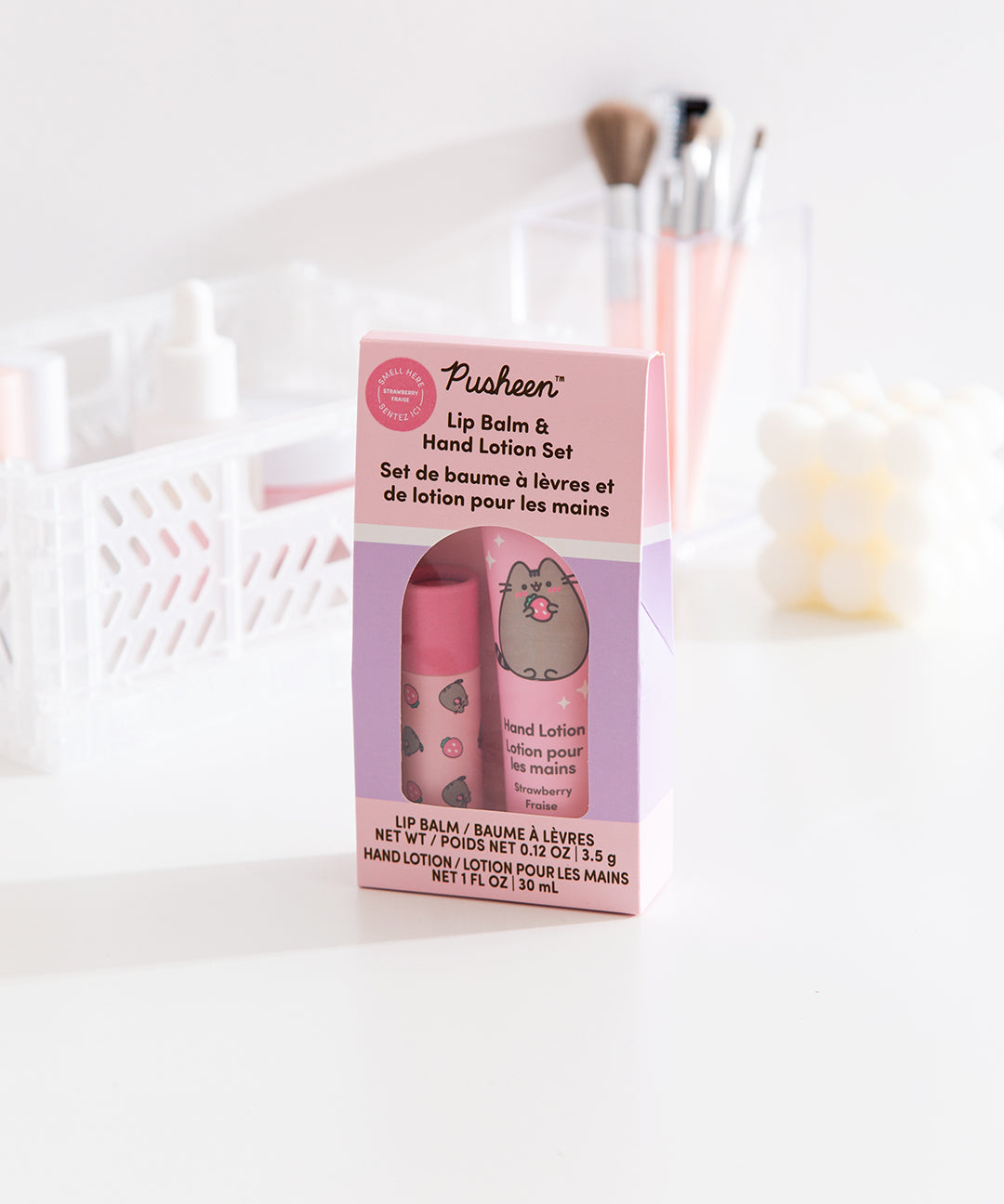Front and side view of the Pusheen lip balm and hand lotion set. The packaging is pink and light purple and includes product details such as the size of the included lip balm and lotion. 