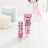 Pusheen strawberry hand lotion and unscented lip balm sit on a white desktop. The set has pink packaging with strawberry graphics. 