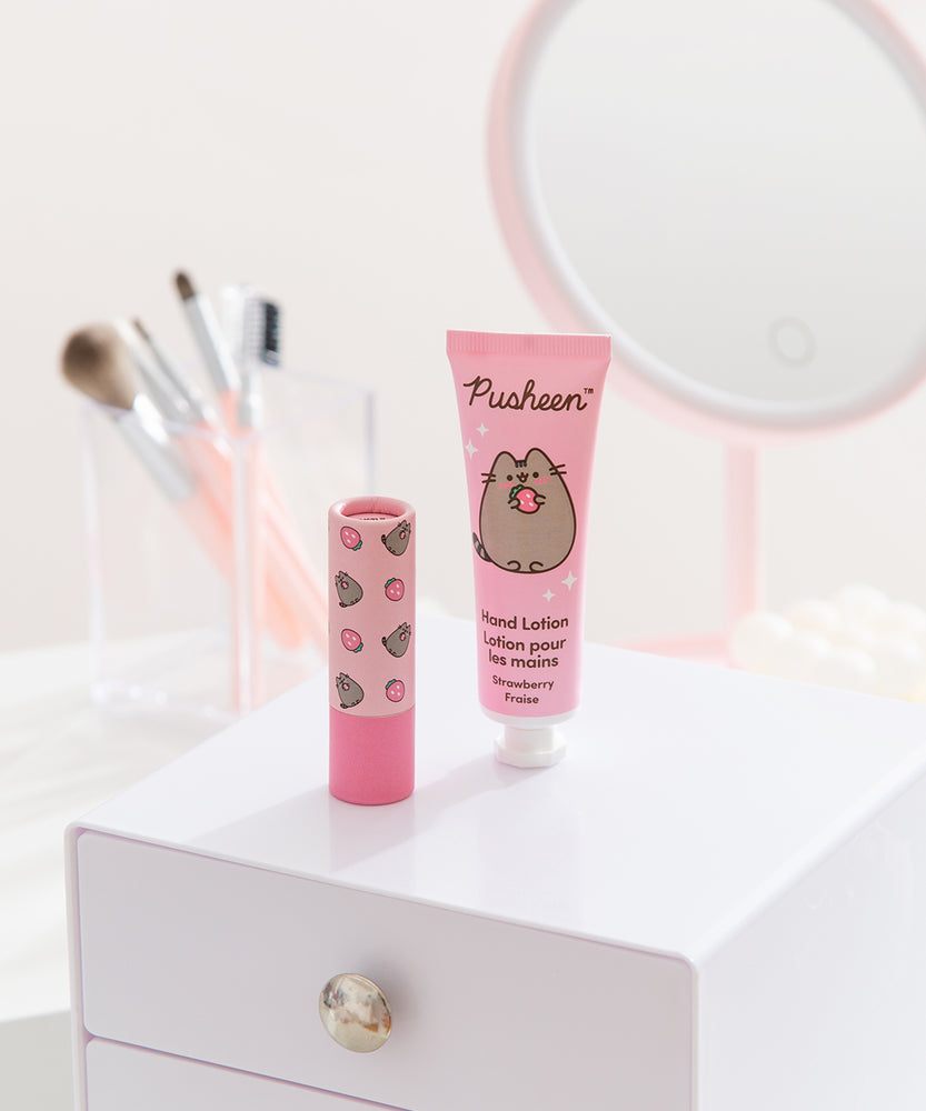 Hand lotion and Pusheen lip balm sit on a vanity. The set has pink packaging and is small enough to carry in a purse. 