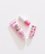 Lip balm and lotion lie on a white desktop. The Pusheen-themed set has a strawberry scented lotion. 