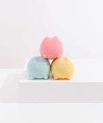 The Pusheen pink squishy toy is stacked onto of the blue and yellow squishy toys that are shaped as a lying down Pusheen the Cat.