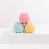 The Pusheen pink squishy toy is stacked onto of the blue and yellow squishy toys that are shaped as a lying down Pusheen the Cat.