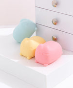 The blue squishy toy rests on the side of a small white drawer set. In front of the blue Pusheen toy are the yellow and pink variations included in this surprise set.