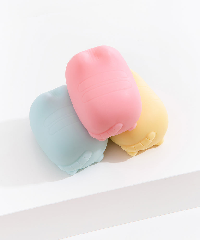 Aerial and back view of the Pusheen surprise squishy toys. Pusheen's classic head stripes, back stripes, and striped tail are embossed in the gel-filled toys.