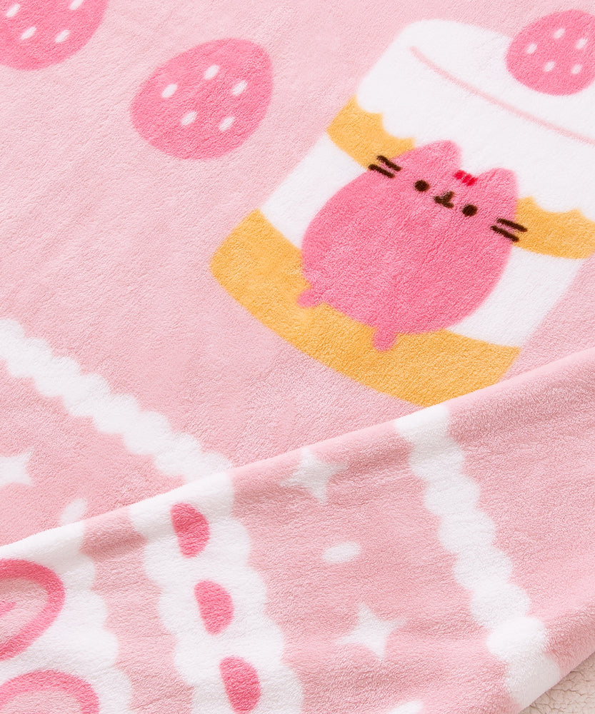 Close-up view of the polyester fabric on the Pusheen Sweet Blanket. The soft pink fabrice has white, medium pink, and light pink graphic details around the border.