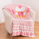 Pusheen Sweets blanket rests on a chair. The center graphic shows a pink Pusheen sitting inside a yellow and white layered cake with a pink strawberry on top.