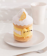 Side quarter view of the lemon Pusheen plush. The cake plush has a light brown cake layer in the middle and at the bottom. The interior lemon custard is accompanied by a wavy whipped cream layer. 