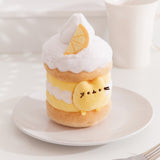 Side quarter view of the lemon Pusheen plush. The cake plush has a light brown cake layer in the middle and at the bottom. The interior lemon custard is accompanied by a wavy whipped cream layer. 