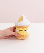 Model's hand holding Pusheen Sweets Lemon Cake Plush 2-pc Environment. The lemon cake plush has a layered cylinder base with whipped topping.