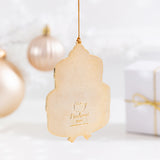 Back view of the ornament, which is a solid gold. The design on the back is the Pusheen the Cat logo and the copyright information. The cake shaped ornament hangs by its gold string in front of a Christmas ornaments and gift box. 