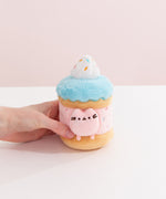 Model's hand holding Pusheen Sweets Sprinkle Cake Plush 2-pc Environment. The birthday cake plush has a layered cylinder base with whipped topping.