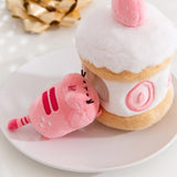 Side view of the Strawberry Plush. The removable interior plush rests in front of the cake environment. The little pink plush has white strawberry seeds embroidered on the booty area of the cat.  