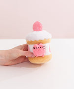 Model's hand holding Pusheen Sweets Strawberry Cake Plush 2-pc Environment. The strawberry cake plush has a layered cylinder base with whipped topping.