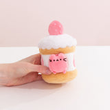 Model's hand holding Pusheen Sweets Strawberry Cake Plush 2-pc Environment. The strawberry cake plush has a layered cylinder base with whipped topping.