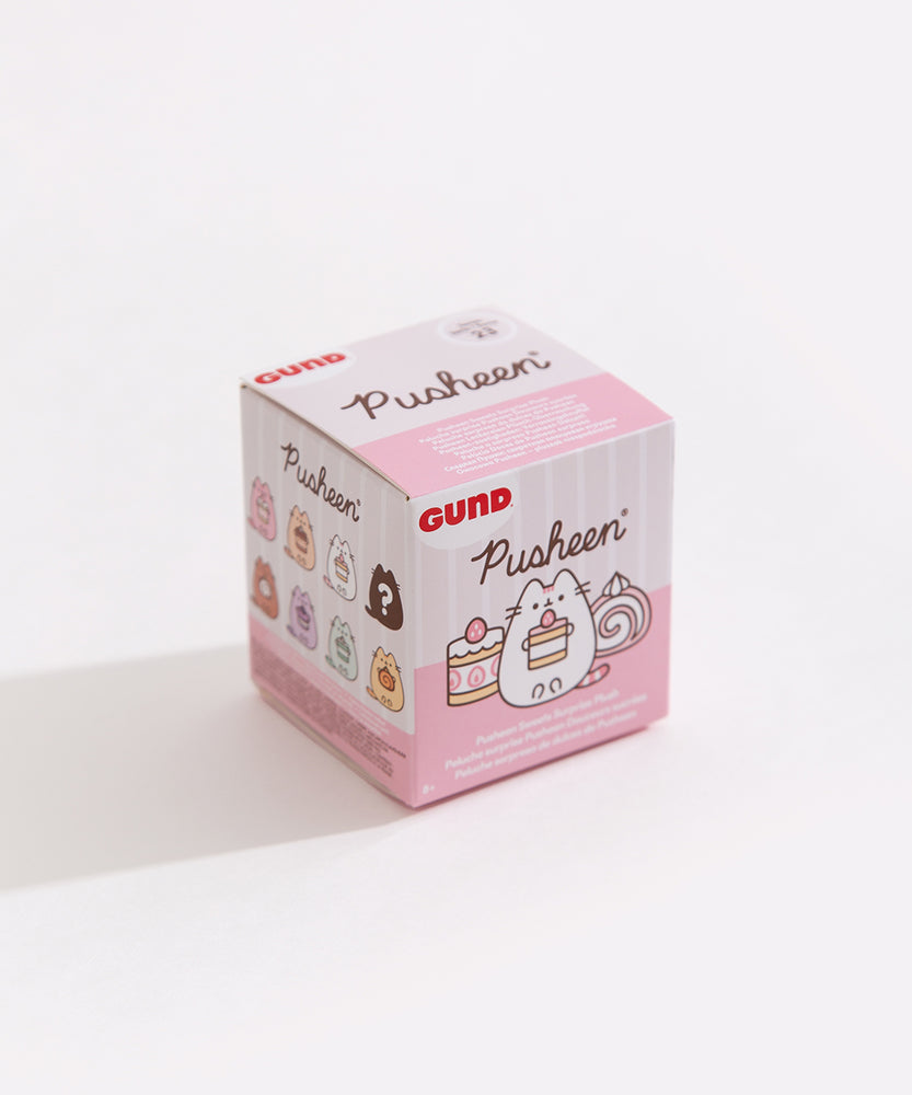 A close-up of the Pusheen Sweets Surprise Plush packaging. The front of the packaging features Pusheen holding a strawberry cake next to another strawberry cake and a cake roll. The side of the box can be seen and it shows the known styles of the blind box series as well as a mystery style.