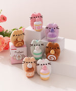 Photo of seven of the plush keychains in the Pusheen Sweets Surprise Plush series. Underneath the caramel roll cake is the blind box packaging for this surprise plush series.