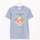 Pusheen Sweets Tee hangs on a light pink hanger on a white background. The light blue tee shirt has a graphic of a box of four macarons with the phrase "Pusheen Sweets" above the graphic and "have a little treat" below the graphic.