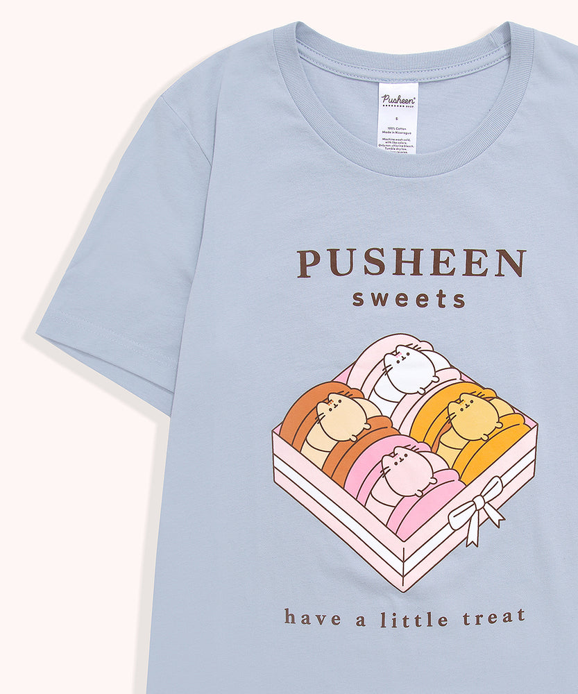 Blue t-shirt with a large graphic on the front center. The graphic shows Pusheen the Cat as four different types of macaron flavors placed in a box.