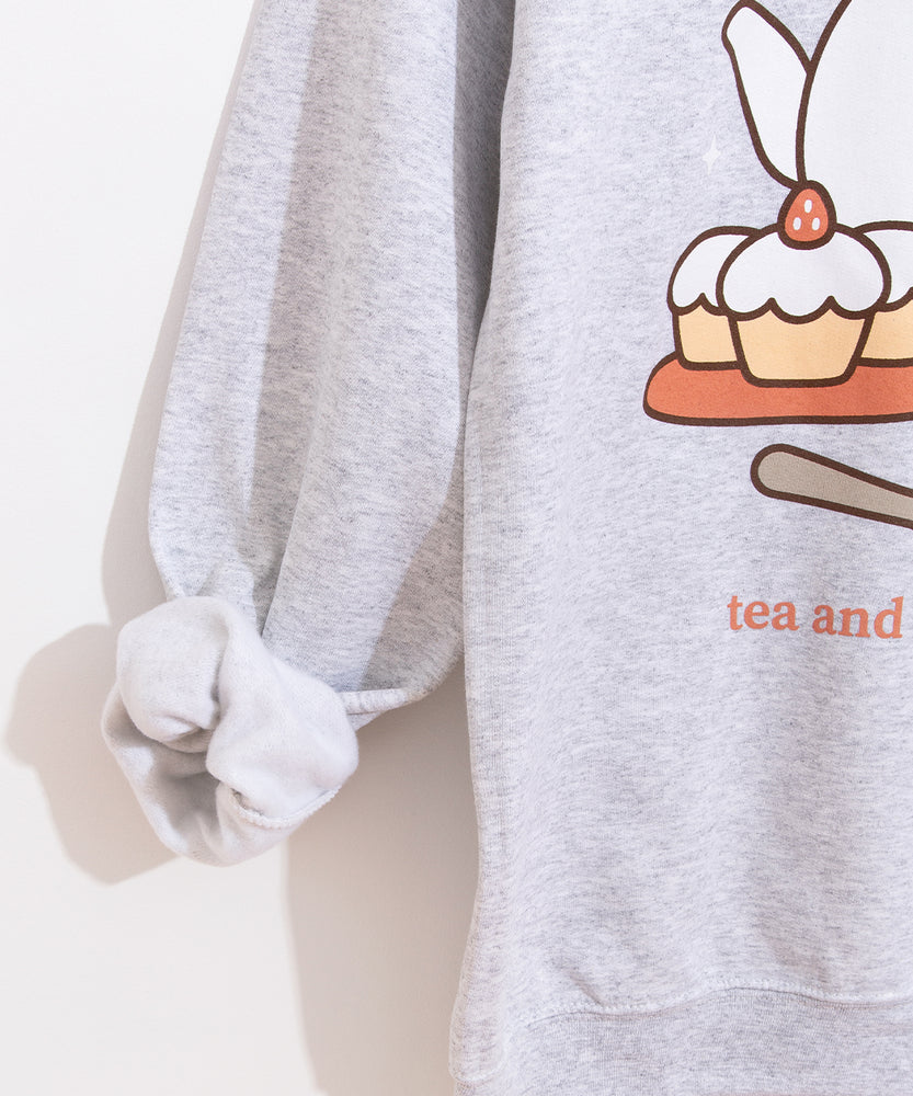 Close-up view of the sleeve and front graphic of the grey unisex sweatshirt. The wearer’s right sleeve is rolled up to reveal the soft interior lining.  