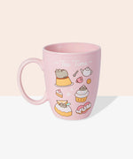 Front view of the Pusheen Tea Time Mug. The light pink mug has a matching light pink handle and interior walls. The outside of the mug features a pattern of Pusheen the Cat with various tea time treats including pudding, cupcakes, biscuits, and cakes. 