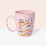 Front view of the Pusheen Tea Time Mug. The light pink mug has a matching light pink handle and interior walls. The outside of the mug features a pattern of Pusheen the Cat with various tea time treats including pudding, cupcakes, biscuits, and cakes. 