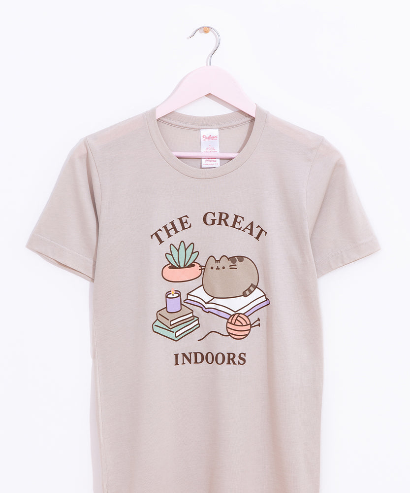 Pusheen Indoors Unisex Tee hangs on a light pink hanger in front of a white background. The printed graphic is placed in the front center of the shirt and covers most of the wearer’s chest. 