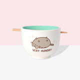 A white ramen bowl with a light teal interior color. The Pusheen graphic shows the gray and brown tabby cat lying with her belly up. Pusheen is shown in her classic form with brown eyes, mouth, and whiskers. She also has a grey striped tail and stripes on her head and back.  