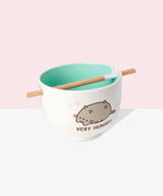 A white ramen bowl with a light teal interior color. The Pusheen graphic shows the gray and brown tabby cat lying with her belly up. Pusheen is shown in her classic form with brown eyes, mouth, and whiskers. She also has a grey striped tail and stripes on her head and back.  