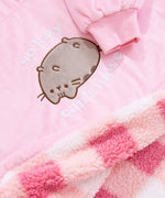 Close-up view of front pocket textured detail and interior sherpa lining. Pusheen the Cat is shown lying on her back surrounded by the phrase “so lazy, can’t move.” The cat is embroidered in brown thread and has a soft grey fur texture for her body. The text is white and is a soft flocked texture. The interior lining of the hoodie is a multi-pink checkered pattern. 