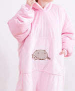 Model wears blanket hoodie. With the sleeves scrunched up, the model holds the side of hood with one hand and has her hand in the large front pocket. The light pink onesie is oversized and lined with sherpa for a cozy fit. 