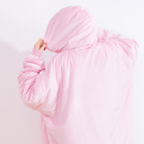 Back view of the model wearing the Wearable Blanket Hoodie. The light pink Pusheen pullover is oversized and the model holds the hood to the side to show the blanket hoodie’s size. 