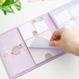 Model holds one sheet of paper in the included notepad. The notepad is pink and features a graphic of Pusheen the Cat holding a pink glazed donut at the bottom of the notepad. 