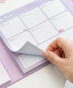 Model picks up one sheet of the weekly planner page in the binder. The planner section includes tear-off pages with squares for each day of the week and weekend. 