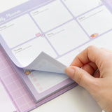 Model picks up one sheet of the weekly planner page in the binder. The planner section includes tear-off pages with squares for each day of the week and weekend. 