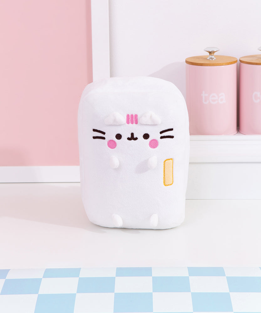 Front view of the Pusheen's Kitchen Refrigerator Plush. The white rectangular plush features Pusheen as a refrigerator with a yellow handle. Pusheen's blush and three head stripes are embroidered in a pink color while her eyes, mouth, and whiskers are embroidered in a dark brown color towards the top of the rectangular plush.