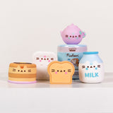 Front view of all Pusheen's Kitchen Surprise Squishy including the blind box capsule. The Squishys include a purple tea pot, white refrigerator, stack of pancakes, bread slice, and white milk bottle.
