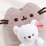 Close up view of the 2-in-1 plush featuring a grey Pusheen the Cat holding a white Kai bear from GUND. Pusheen's facial features are embroidered in brown and dark grey. The white anniversary plush bear features a cream colored snout and brown nose.